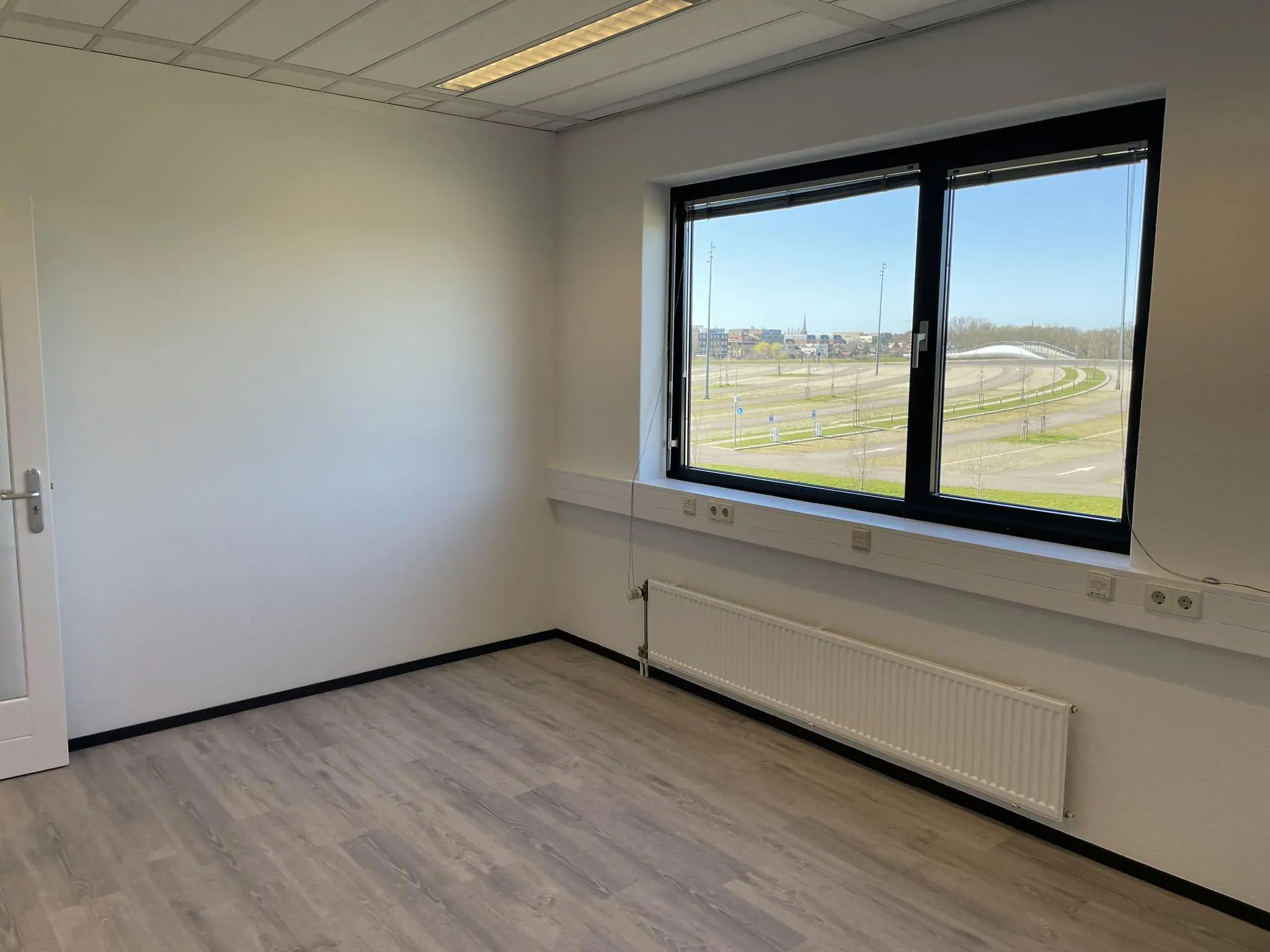 Leeg kantoor met laminaatvloer en groot raam met uitzicht op de Laan van S-Gravenmade.